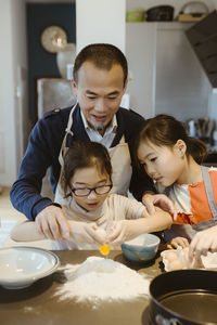 Father teaching daughter to break egg in flour while preparing food at home