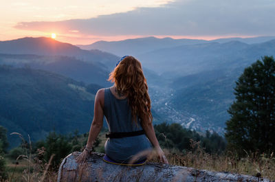 A girl sits on the edge of the cliff and looking at the sun valley and mountains. woman sitting 