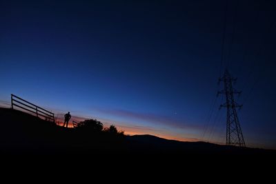 Silhouette electricity pylons on landscape against clear sky