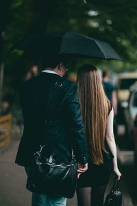 Rear view of couple walking on footpath during rain