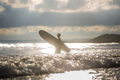 Silhouette man carrying surfboard in sea