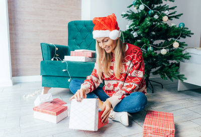 Smiling woman wearing santa hat opening christmas presents