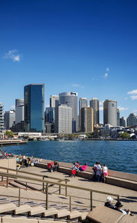 People in city by sea against blue sky