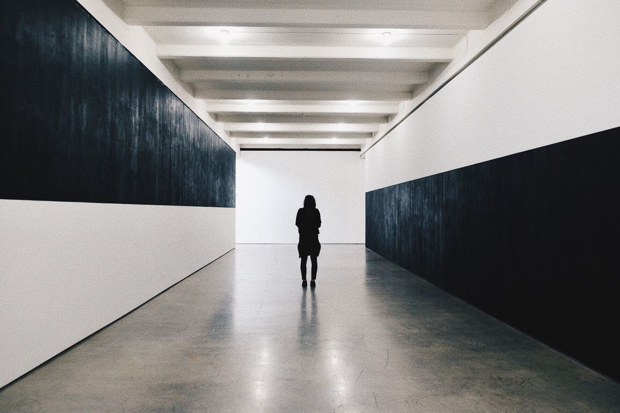 architecture, the way forward, rear view, direction, walking, indoors, arcade, real people, corridor, illuminated, building, one person, wall - building feature, lifestyles, built structure, full length, lighting equipment, diminishing perspective, ceiling, flooring, underground walkway, light fixture