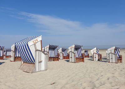 Hooded chairs on beach against sky