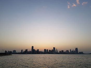 Sea by buildings against sky during sunset