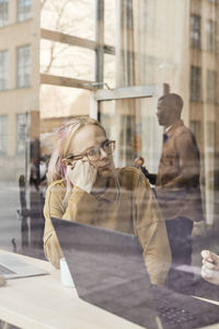 Young non-binary entrepreneur sitting in tech start-up office seen through glass window