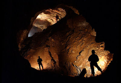 Silhouette people standing in cave at night