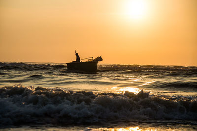 Silhouette man in boat on sea against sky during sunset