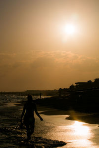 Silhouette man standing on beach against sky during sunset