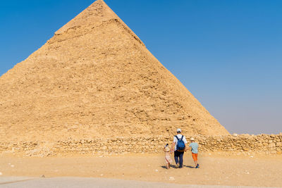 Father and children walk in front of the chephren pyramid on the giza plateau