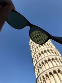 Low angle view of hand holding built structure against blue sky