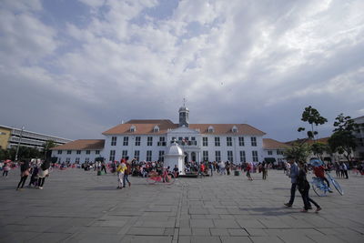 People on street amidst buildings in city against sky