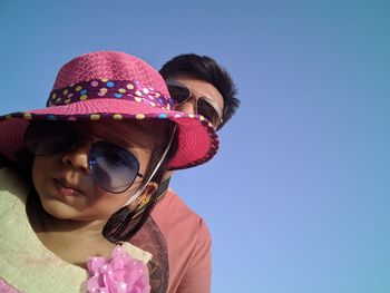 Portrait of father and daughter wearing sunglasses against clear blue sky