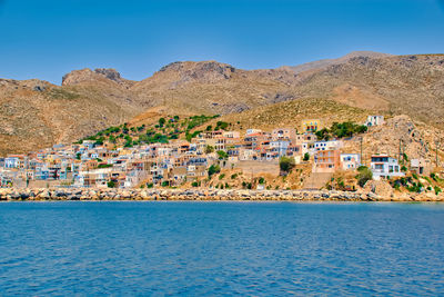 Scenic view of town by mountains against clear blue sky