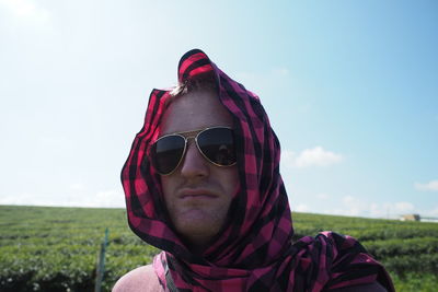 Portrait of young man wearing sunglasses on field against sky