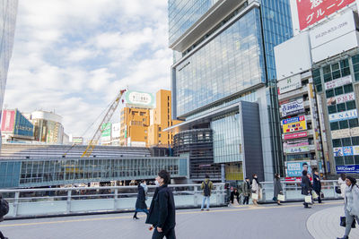 People walking on city street by modern buildings against sky