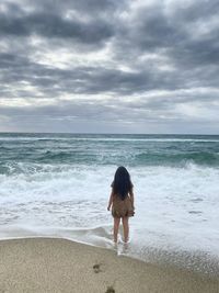 Rear view of woman on beach against sky