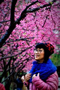 Thoughtful woman smiling while standing against pink cherry blossoms