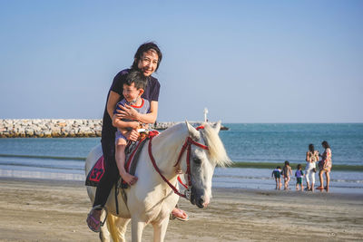 Happy woman with son riding horse at beach