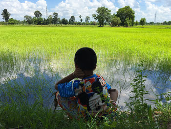 Rear view of boy crouching at rice paddy