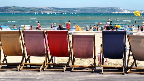 People enjoying at beach with deck chairs in foreground