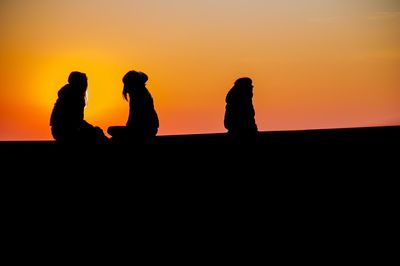 Silhouette people against orange sky during sunset