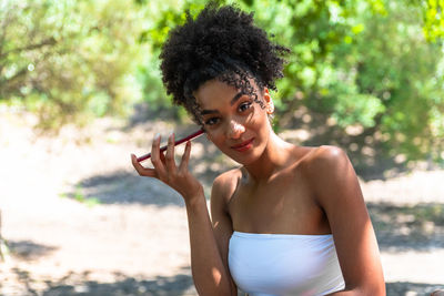 Portrait of young woman holding camera while standing outdoors