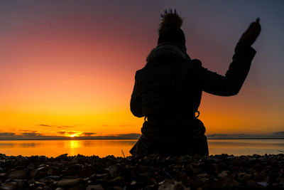 Rear view of woman on rock at beach during sunset