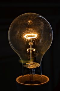 Close-up of illuminated light bulb over black background