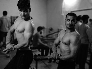 Shirtless male friends flexing muscles in gym