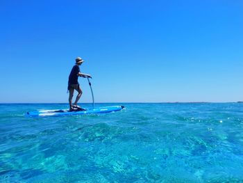 Person on sea with a board stating against blue sky