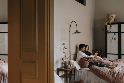 Boyfriend sharing smart phone with non-binary person sitting in bedroom at home