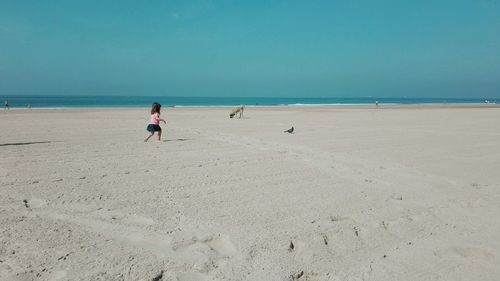 Side view of girl running at beach against clear blue sky during sunny day