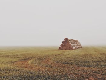 Stack of hay bales on grassy field against clear sky during foggy weather