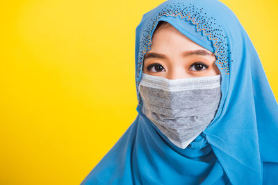 Portrait of young woman wearing mask against yellow background