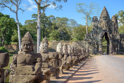 Statues by road against trees at angkor thom south gate