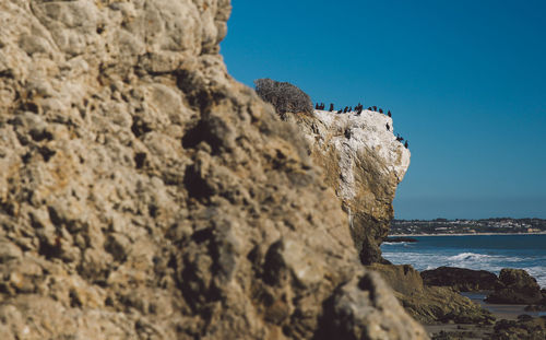 Rock formation by sea against clear blue sky