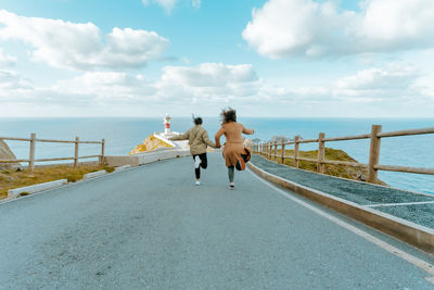 Rear view of women on railing by sea against sky