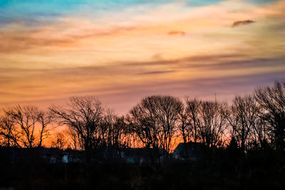 Silhouette trees on field against dramatic sky during sunset