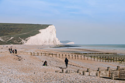 People at beach against cliff and sky