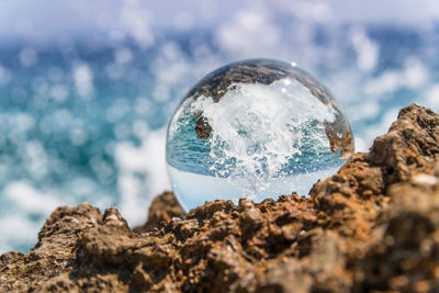 Close-up of crystal ball on rock against sea