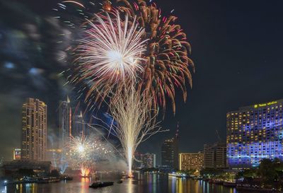 Firework display over illuminated city against sky at night