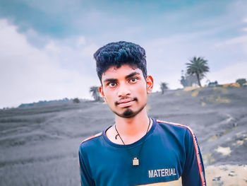 Portrait of young man standing on land against sky