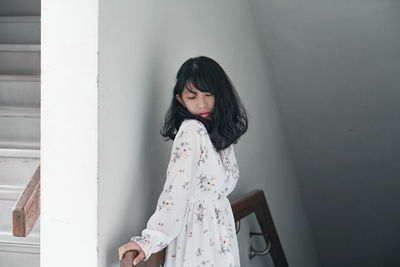 Young woman looking away while standing against wall