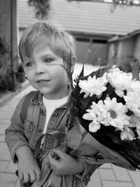 Cute boy holding flower bouquet while standing outdoors