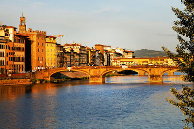 Arch bridges over arno river by buildings against sky