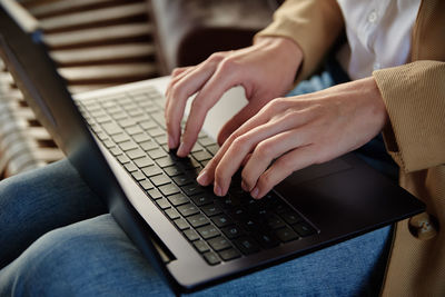 Woman sitting on bench and typing on laptop keyboard