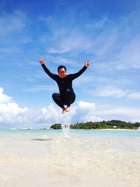 Man with arms outstretched jumping in mid-air over sea against blue sky