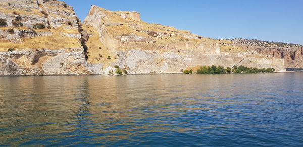 Rock formations by sea against clear blue sky